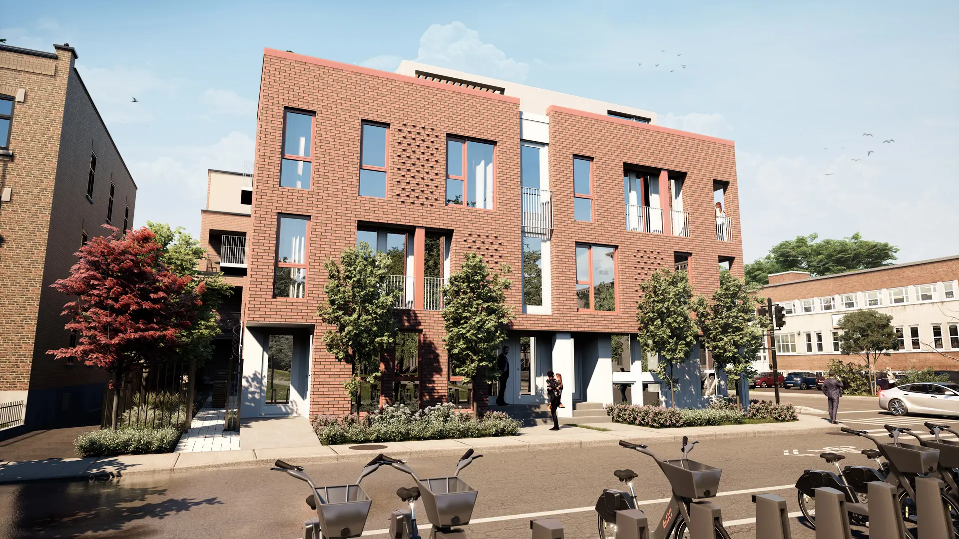 Un immeuble moderne de trois étages en briques avec de grandes fenêtres, des arbres bordant le trottoir et des vélos de location garés sur un support à vélos au premier plan. Deux personnes se tiennent près de l'entrée.